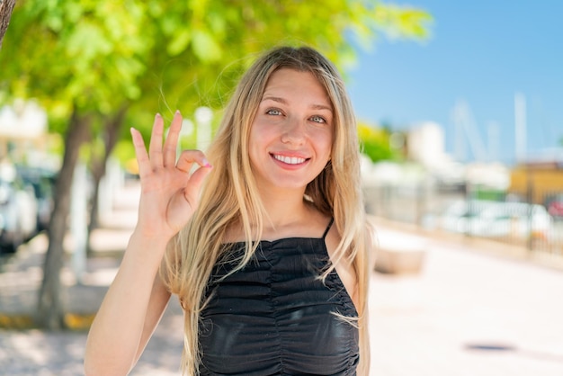 Mujer rubia joven al aire libre mostrando signo ok con los dedos