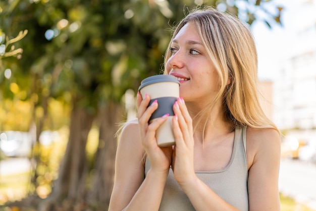 Mujer rubia joven al aire libre sosteniendo un café para llevar