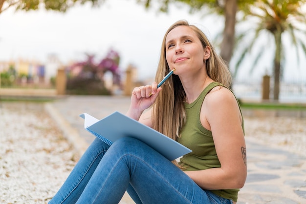 Mujer rubia joven al aire libre sosteniendo un cuaderno