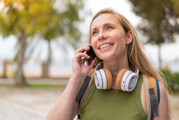 Mujer rubia joven al aire libre usando teléfono móvil