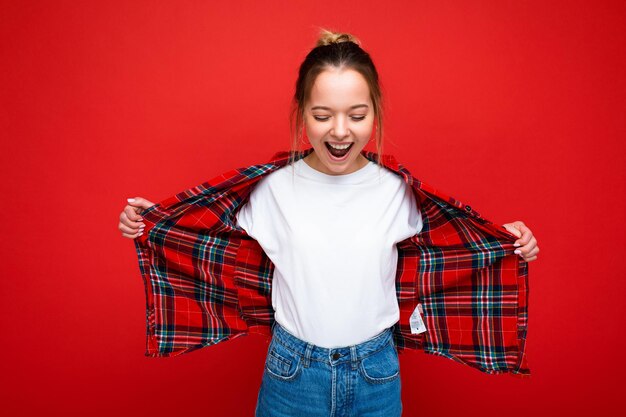 Mujer rubia joven atractiva sorprendida feliz inconformista en elegante camisa roja y camiseta blanca casual