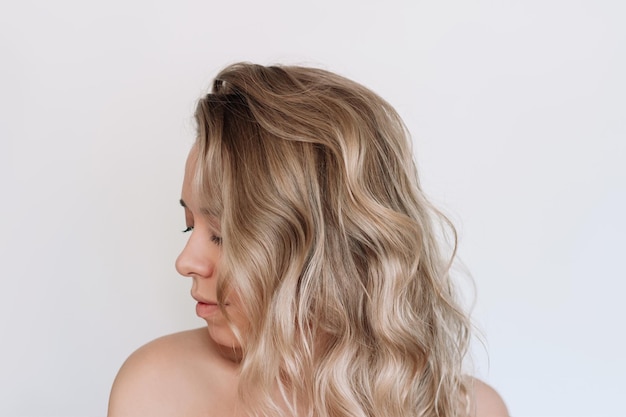 Foto mujer rubia joven con cabello ondulado voluminoso sobre un fondo blanco resultado de la coloración del cabello