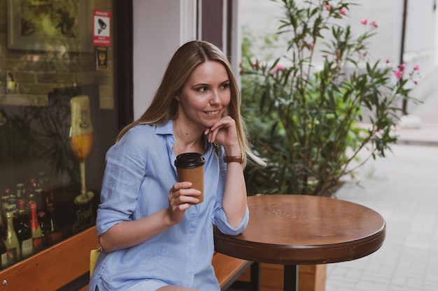 Mujer rubia joven con café en un café de la calle en verano