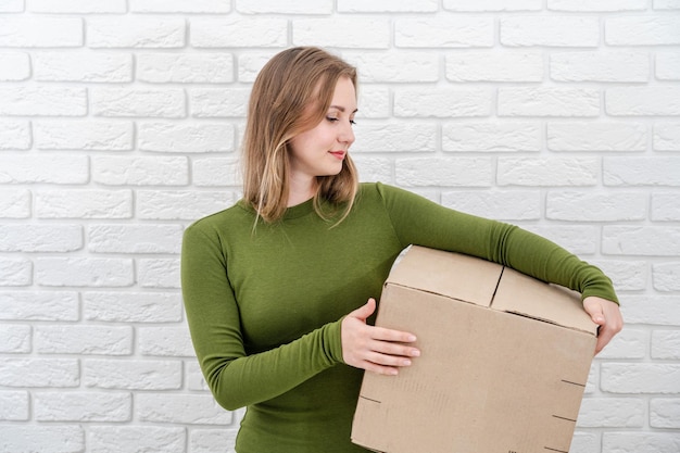 Mujer rubia joven con caja de paquetes entregando un paquete