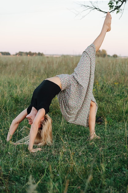 Mujer rubia joven en un campo de pie en pose de puente con la pierna levantada