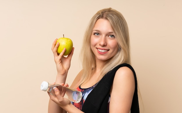 Mujer rubia joven del deporte con una manzana y una botella de agua