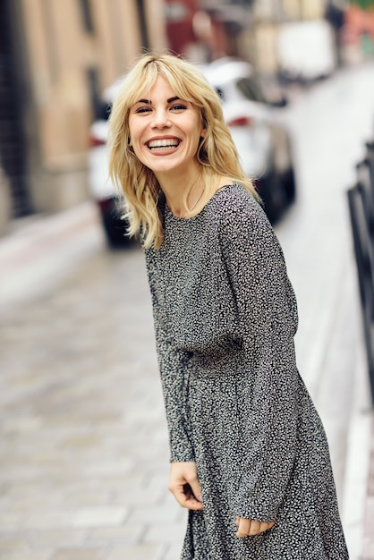 Mujer rubia joven divertida que se coloca en fondo urbano.