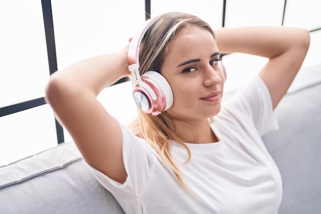 Mujer rubia joven escuchando música relajada en el sofá en casa