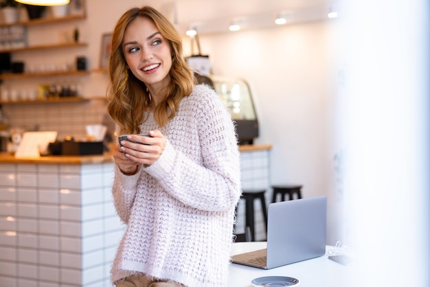 una mujer rubia joven feliz alegre positiva que presenta en la cafetería en el interior tomando café.