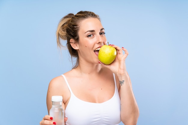 Mujer rubia joven feliz con una manzana y una botella de agua