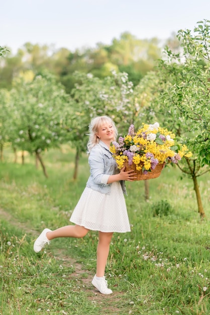 Mujer rubia joven con una gran cesta de flores en el jardín de primavera