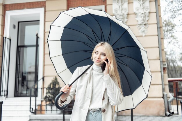 Mujer rubia joven hablando por teléfono con paraguas