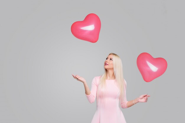 Mujer rubia joven hermosa con el globo rosado de la forma del corazón en gris. Mujer en el día de San Valentín. Símbolo del amor - Imagen. Espacio para texto