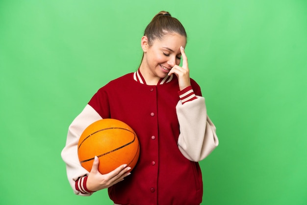 Mujer rubia joven jugando baloncesto sobre fondo clave de croma aislado riendo