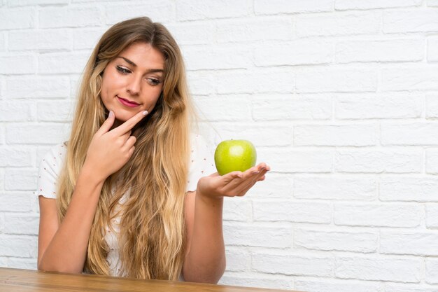 Foto mujer rubia joven con una manzana pensando