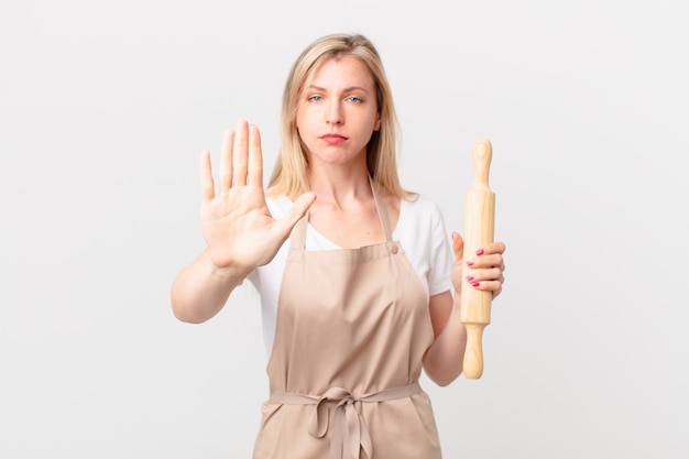 Mujer rubia joven que parece seria que muestra la palma abierta que hace el gesto de la parada. concepto de panadero