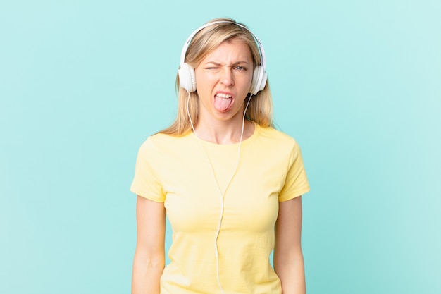 Mujer rubia joven que se siente disgustada e irritada y con la lengua fuera y escuchando música.