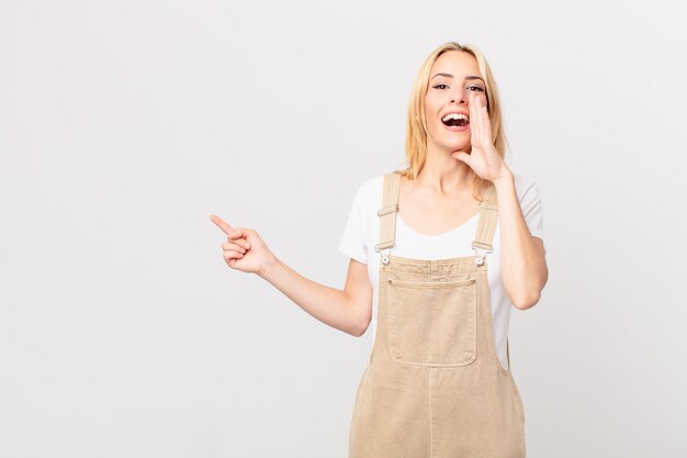 Mujer rubia joven que se siente feliz, dando un gran grito con las manos al lado de la boca