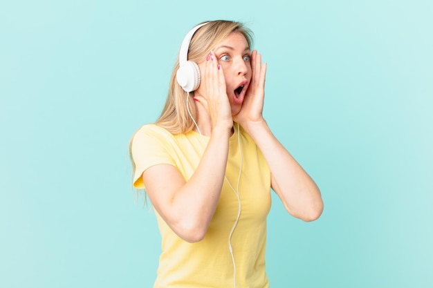 Mujer rubia joven que se siente feliz, emocionada y sorprendida y escuchando música.