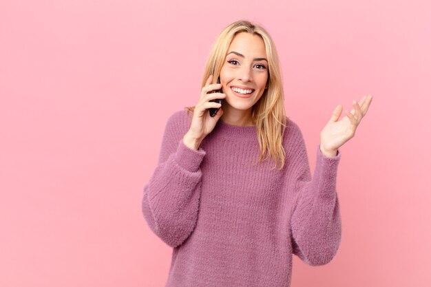 Mujer rubia joven que se siente feliz, sorprendida al darse cuenta de una solución o idea y hablando con un teléfono inteligente