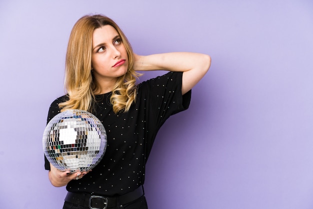 La mujer rubia joven que sostenía una bola del partido de la noche aisló tocar la parte posterior de la cabeza, pensar y tomar una decisión.