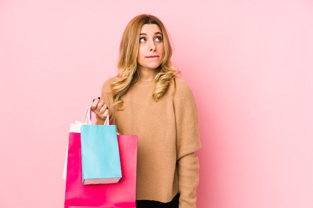 Mujer rubia joven que sostiene bolsas de la compra aisladas confundidas, se siente dudosa e insegura.