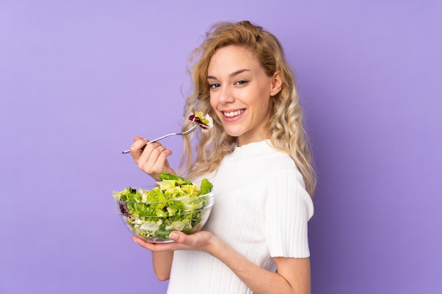 Mujer rubia joven que sostiene la ensalada en púrpura