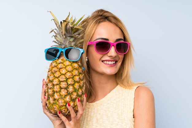 Mujer rubia joven que sostiene una piña con las gafas de sol