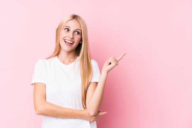 Mujer rubia joven en rosa que sonríe alegremente que señala con el índice lejos.