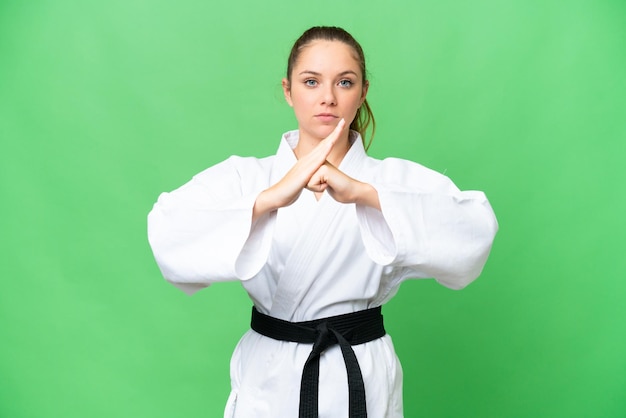 Mujer rubia joven sobre fondo clave de croma aislado haciendo karate y saludando