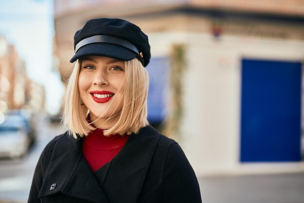 Mujer rubia joven sonriendo feliz de pie en la ciudad.