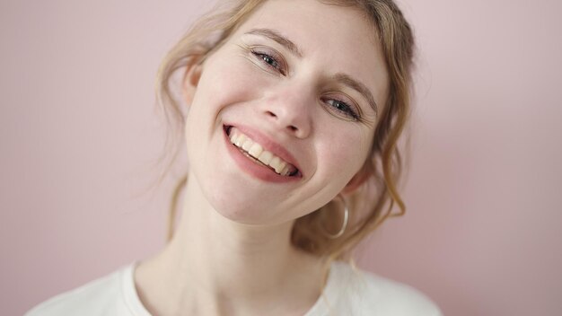 Mujer rubia joven sonriendo segura de pie sobre fondo rosa aislado