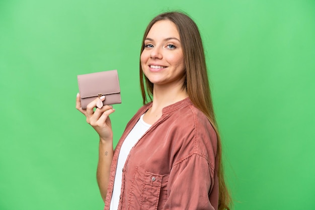 Mujer rubia joven sosteniendo una billetera sobre un fondo clave de croma aislado sonriendo mucho