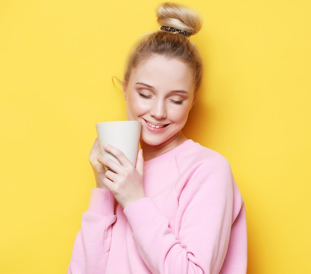 Mujer rubia joven sosteniendo una taza blanca con estilo de vida de té o café y concepto de comida Fondo amarillo