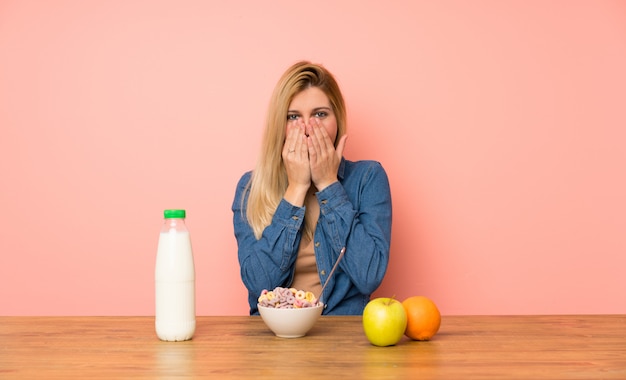 Mujer rubia joven con tazón de cereales con expresión facial sorpresa