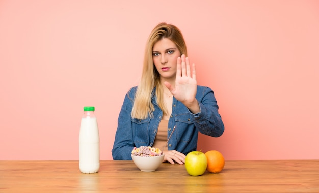 Mujer rubia joven con tazón de cereales haciendo gesto de parada con su mano