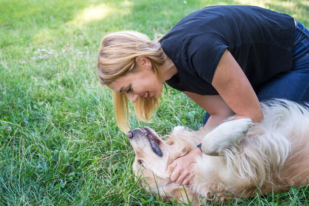 Una mujer rubia juega con un perro Golden Retriever en el césped del parque.