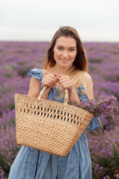 Mujer rubia bajo la lluvia en el campo de lavanda Provenza. Recogiendo flores en la bolsa de mimbre.