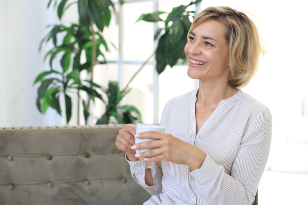 Mujer rubia madura en el sofá tomando un té o un café.