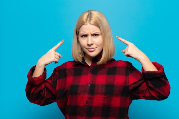 Mujer rubia con mala actitud que parece orgullosa y agresiva, apuntando hacia arriba o haciendo letreros divertidos con las manos