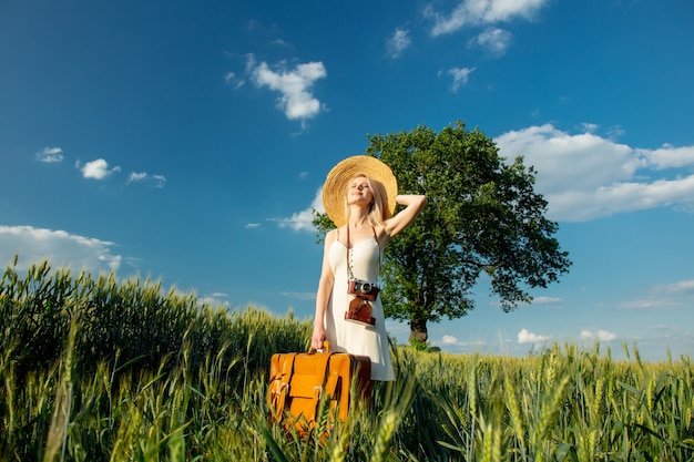 Mujer rubia con maleta y cámara en campo de trigo en verano