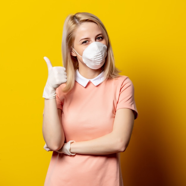 Mujer rubia en mascarilla y vestido rosa en pared amarilla