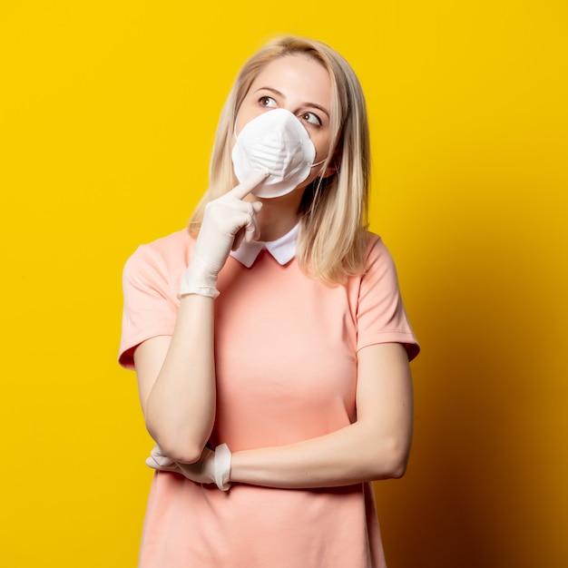 Mujer rubia en mascarilla y vestido rosa en pared amarilla