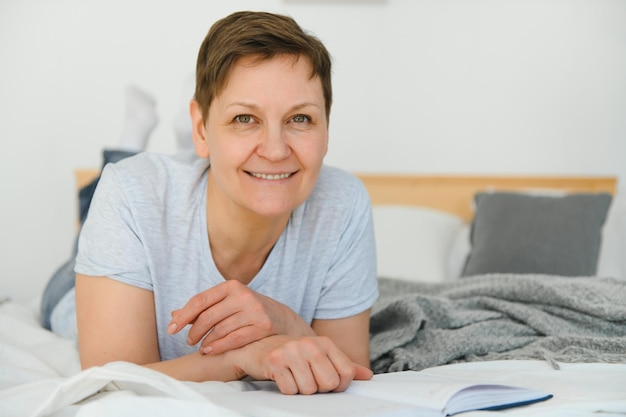 Mujer rubia de mediana edad leyendo un libro acostado en la cama en casa