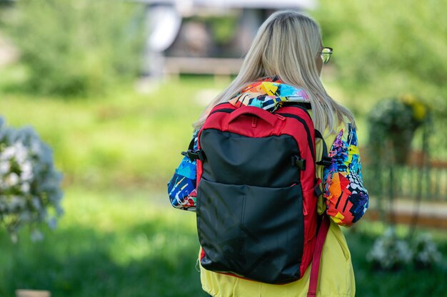 Mujer rubia de mediana edad con ropa brillante con una mochila en el parque en un día soleado vista trasera