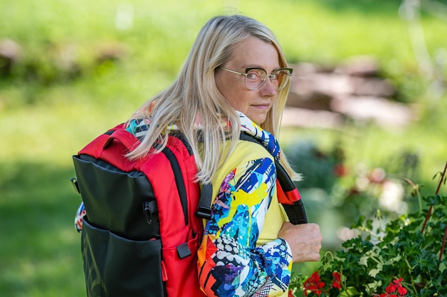 Mujer rubia de mediana edad con ropa brillante con una mochila en el parque en un día soleado vista trasera