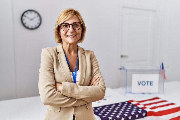 Mujer rubia de mediana edad sonriendo confiada con gesto de brazos cruzados en el colegio electoral