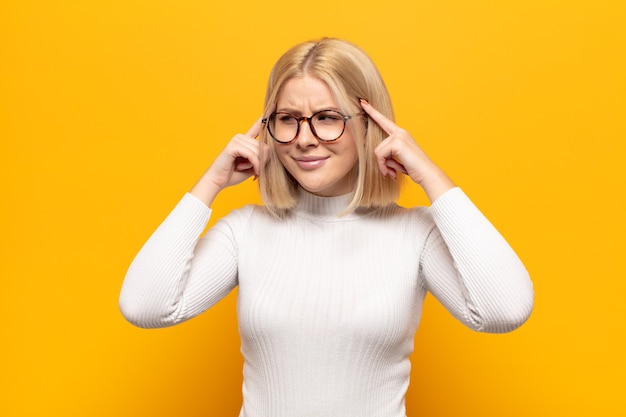 Mujer rubia mirando concentrada y pensando mucho en una idea, imaginando una solución a un desafío o problema