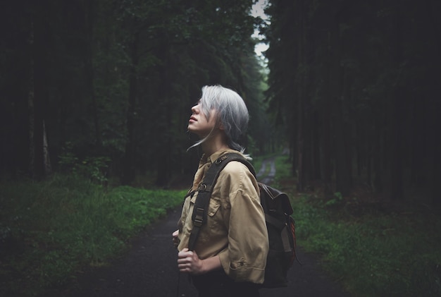 Mujer rubia con mochila en día lluvioso en bosque