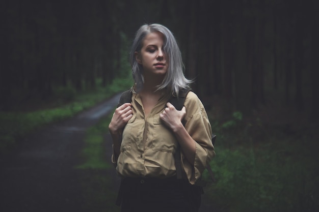 Mujer rubia con mochila en día lluvioso en bosque